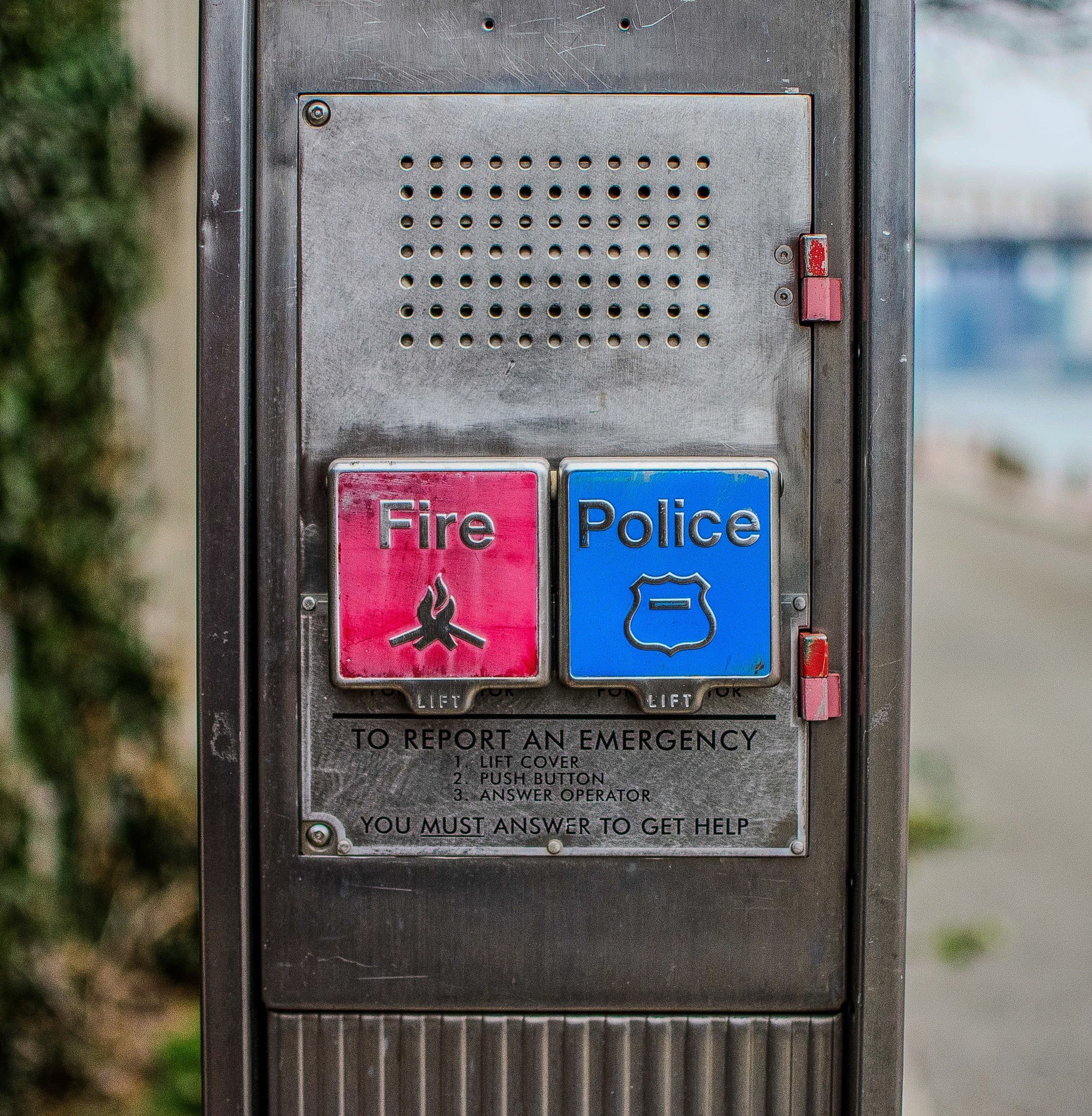 A weathered emergency call box mounted on a brick wall, two buttons — Fire and Police — faded red and blue.