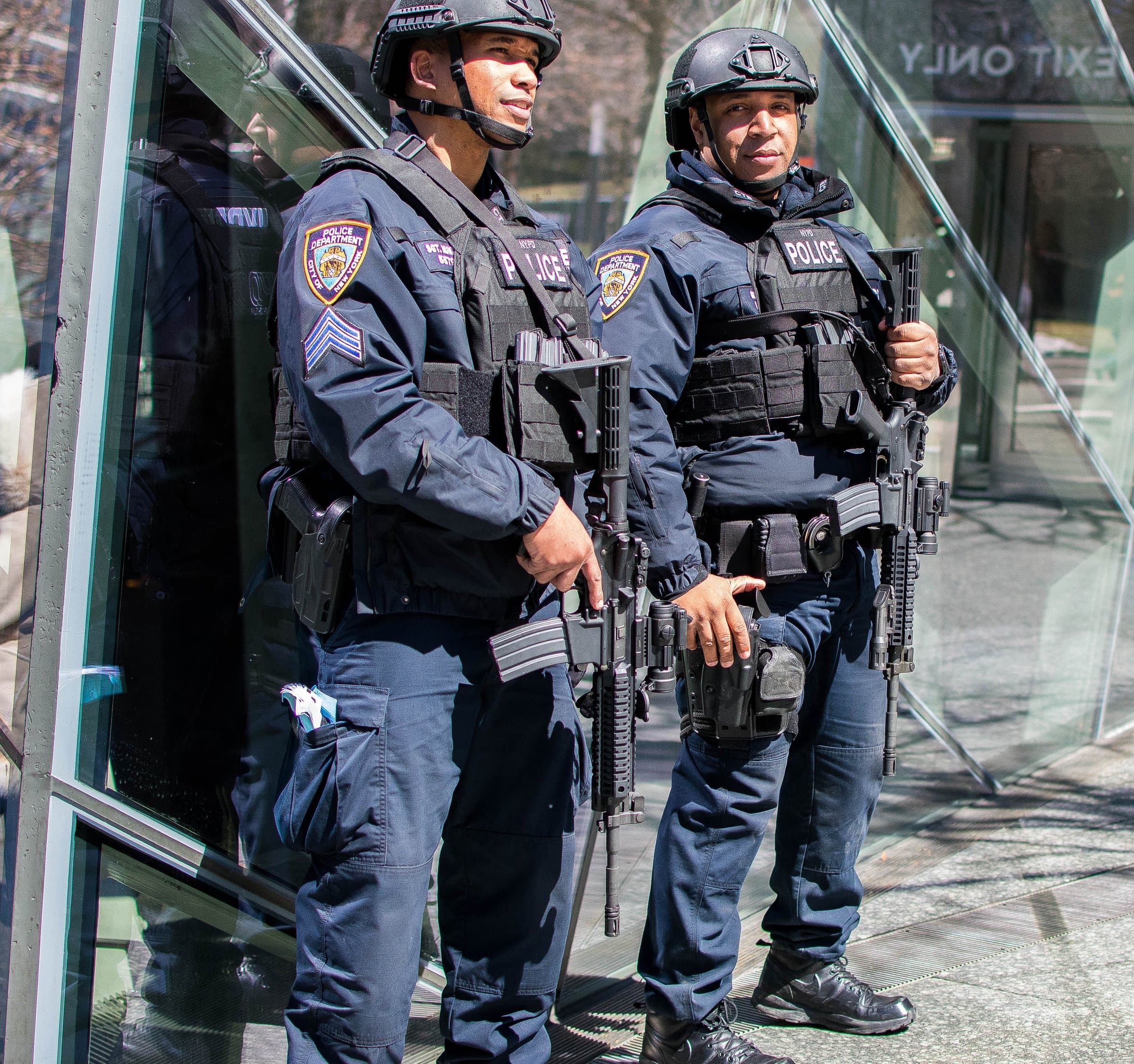Two heavily armed NYPD officers in tactical gear stand at a building entrance in the Financial District.
