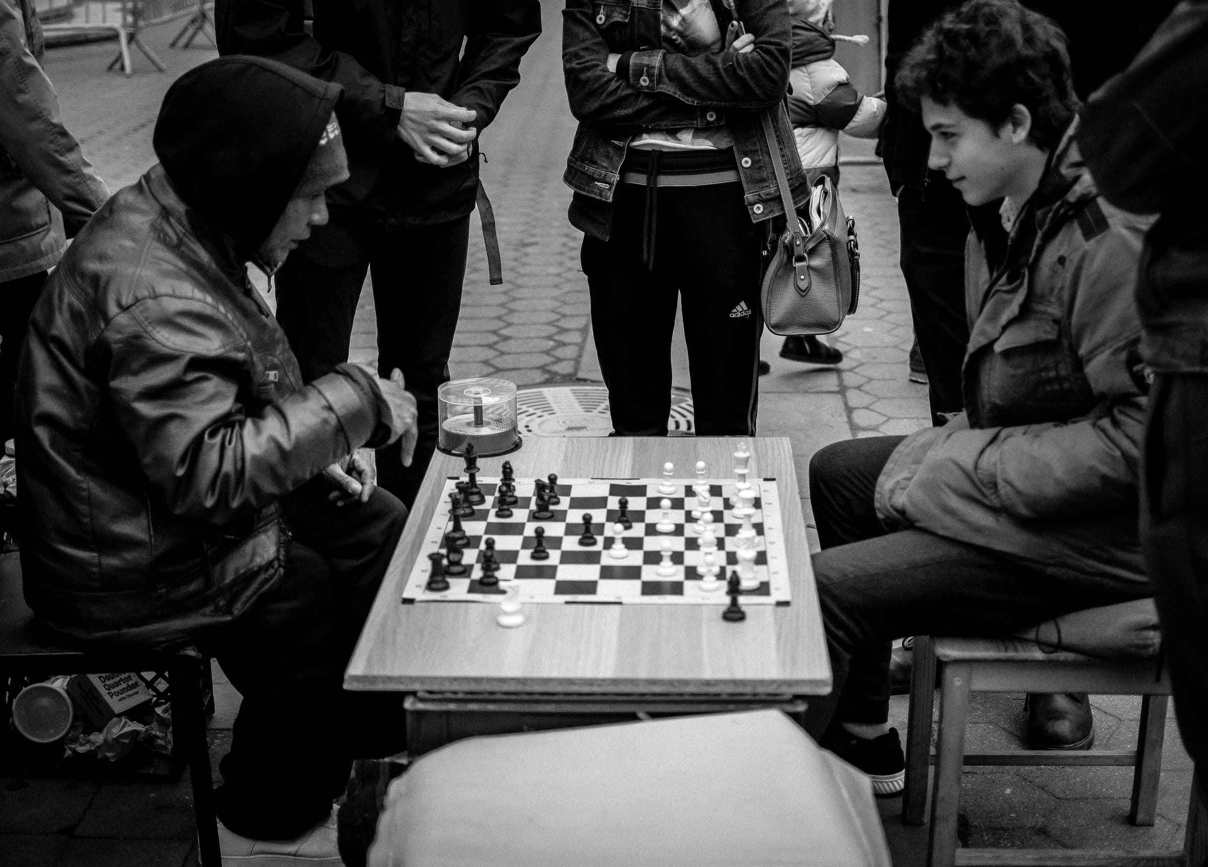 Two men playing chess on a street table in Union Square, a crowd watching