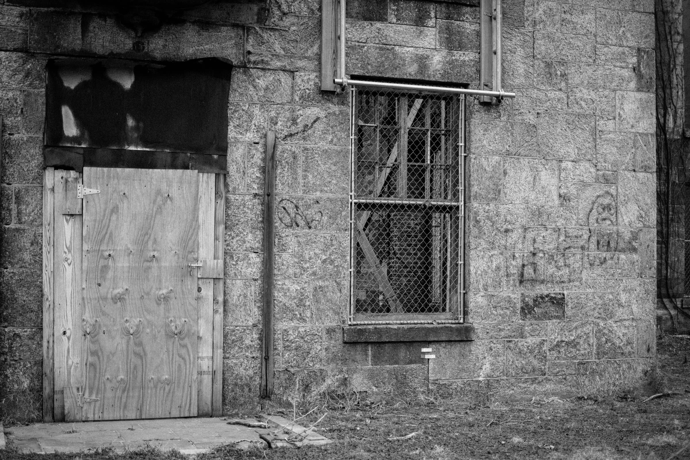 The abandoned Renwick Smallpox Hospital on Roosevelt Island — boarded door, chain-link over a broken window, stone walls.