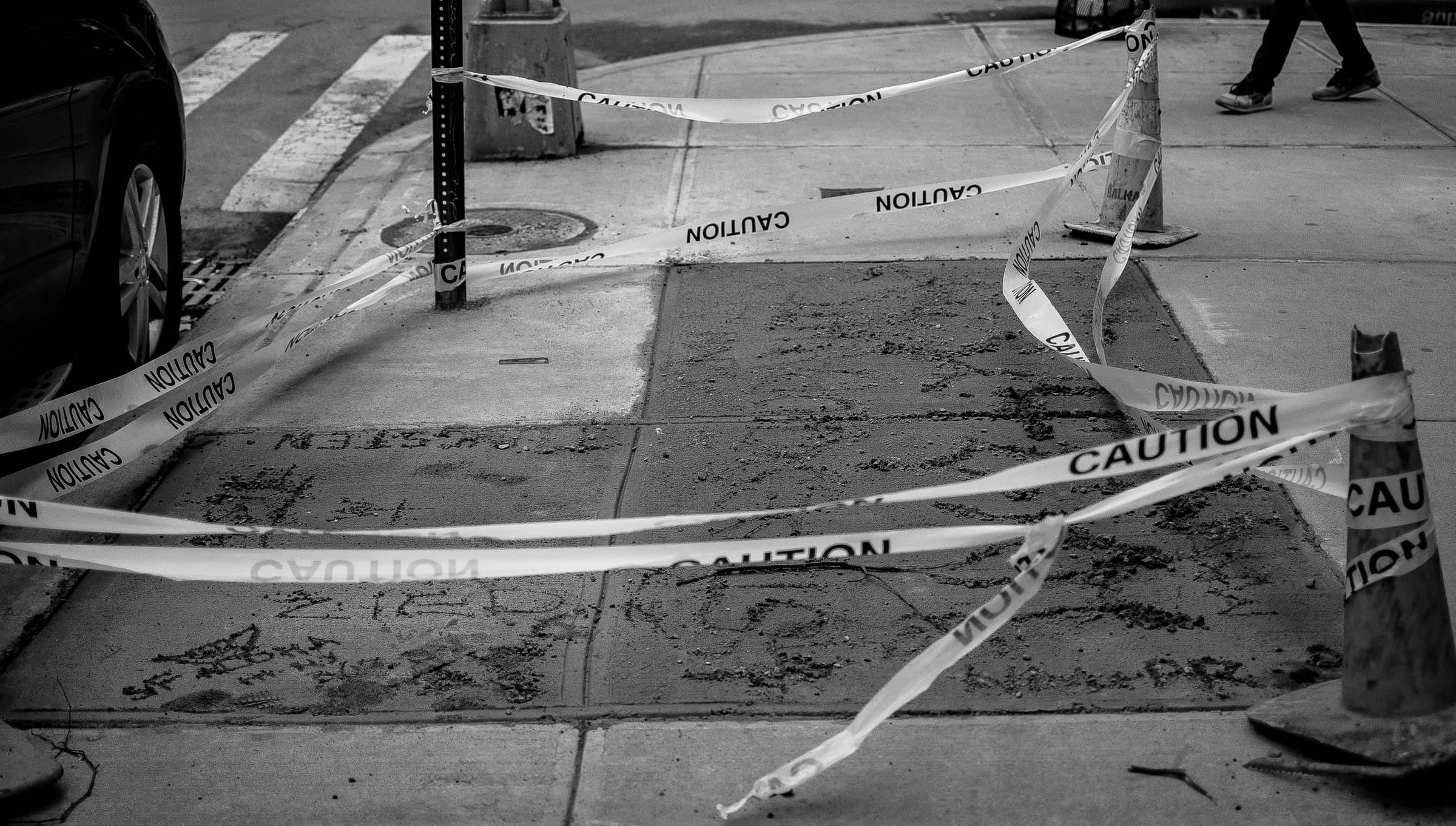 Caution tape lies scattered and ineffective across vandalized concrete sidewalk tiles, black and white